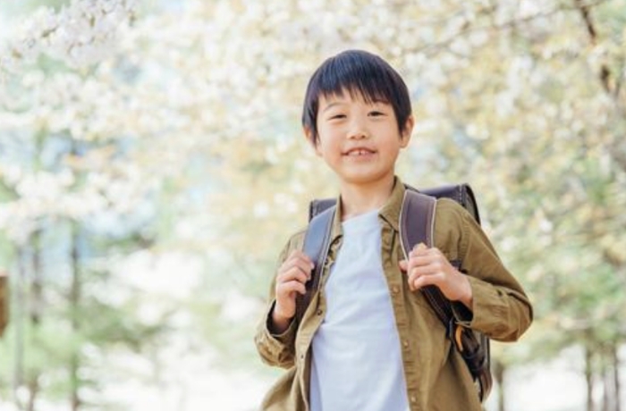 桜の下で笑顔でこちらを向く子ども